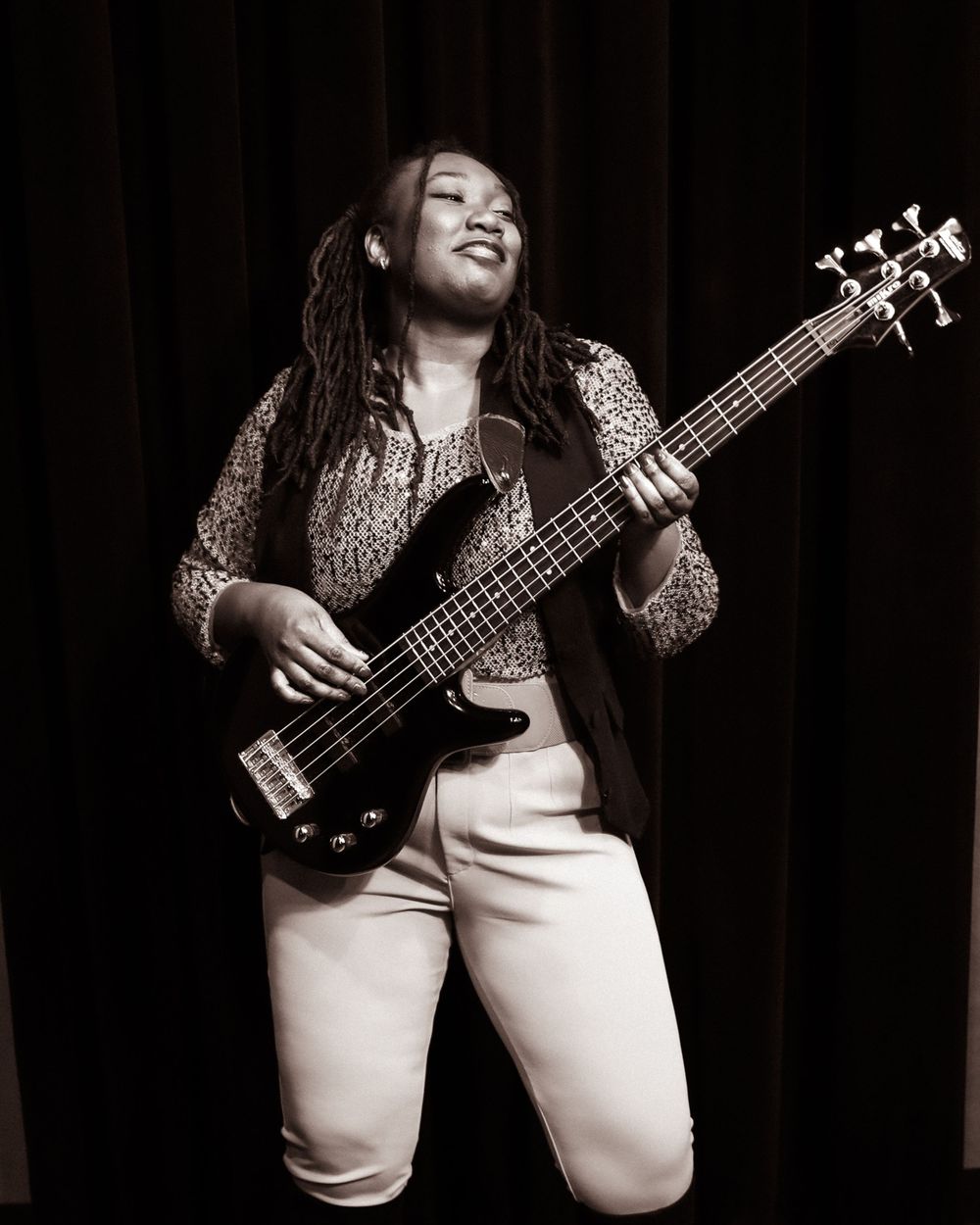 Bass guitarist performing with passion in black and white against a dark curtain background.