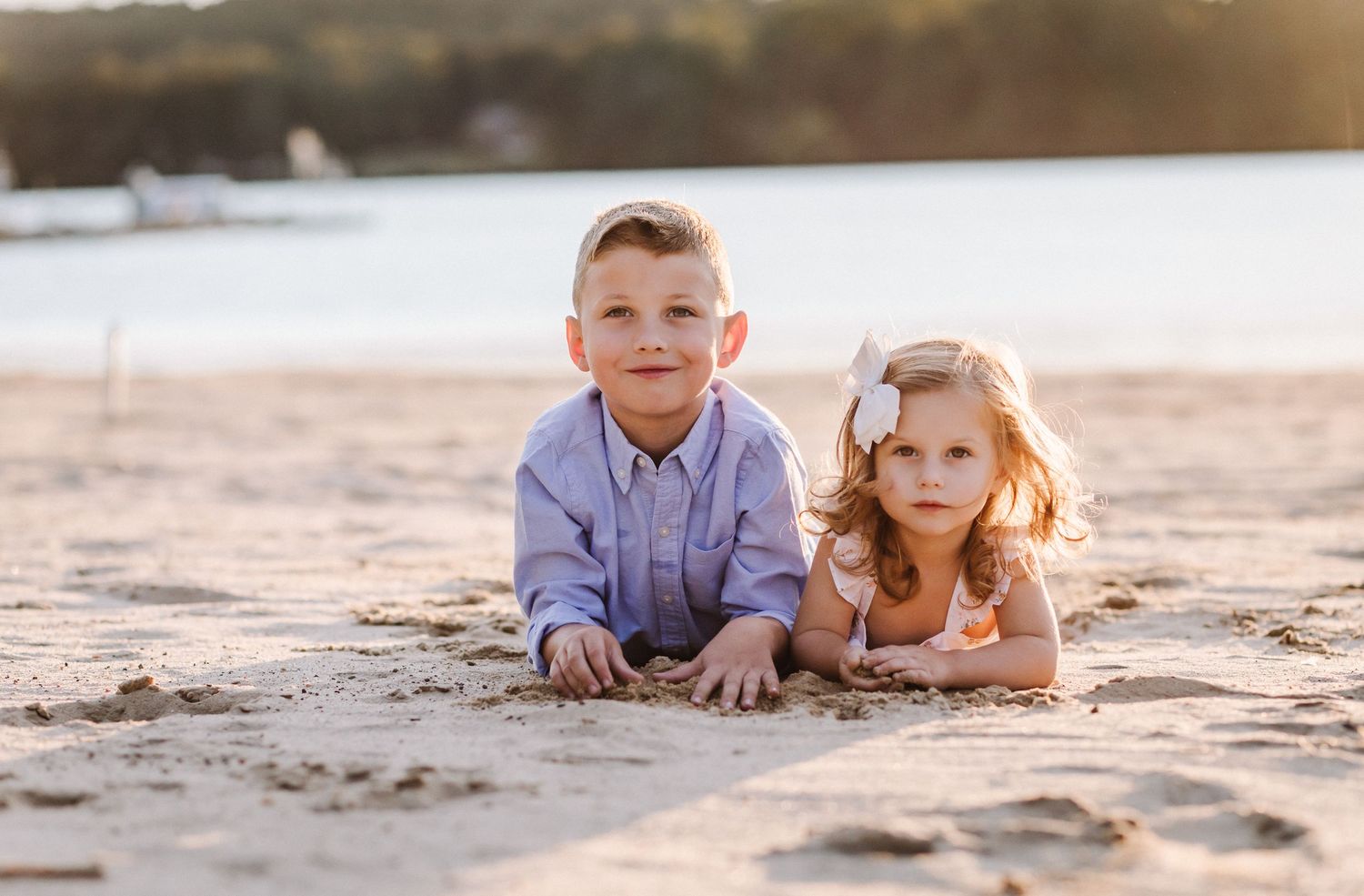 Two children lying on beach sand during golden hour sunset.