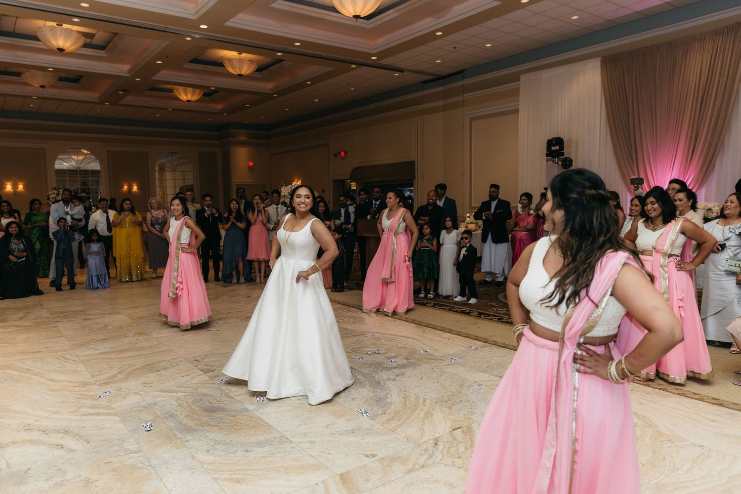 Wedding reception in an elegant ballroom with pink decor and dancing guests.