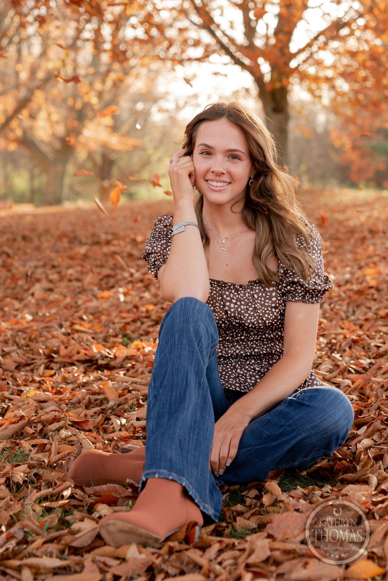 Relaxed autumn portrait sitting in fallen leaves wearing brown print top and denim.