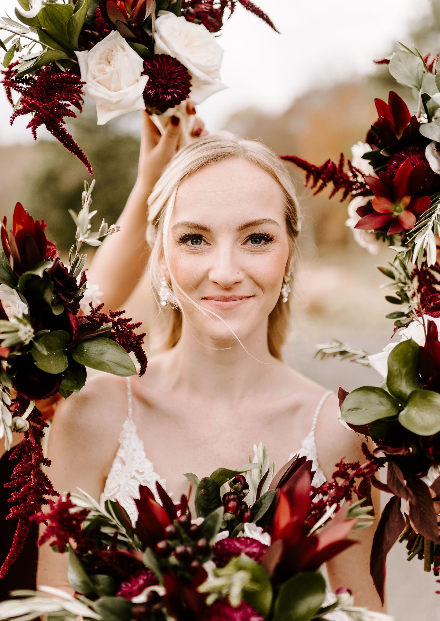 Bride framed by burgundy and blush floral arrangement against soft autumn background.