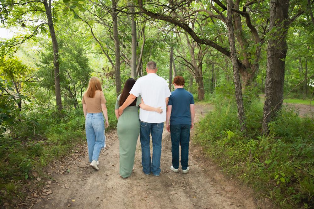 Family walking together on a tree-lined dirt path from behind.