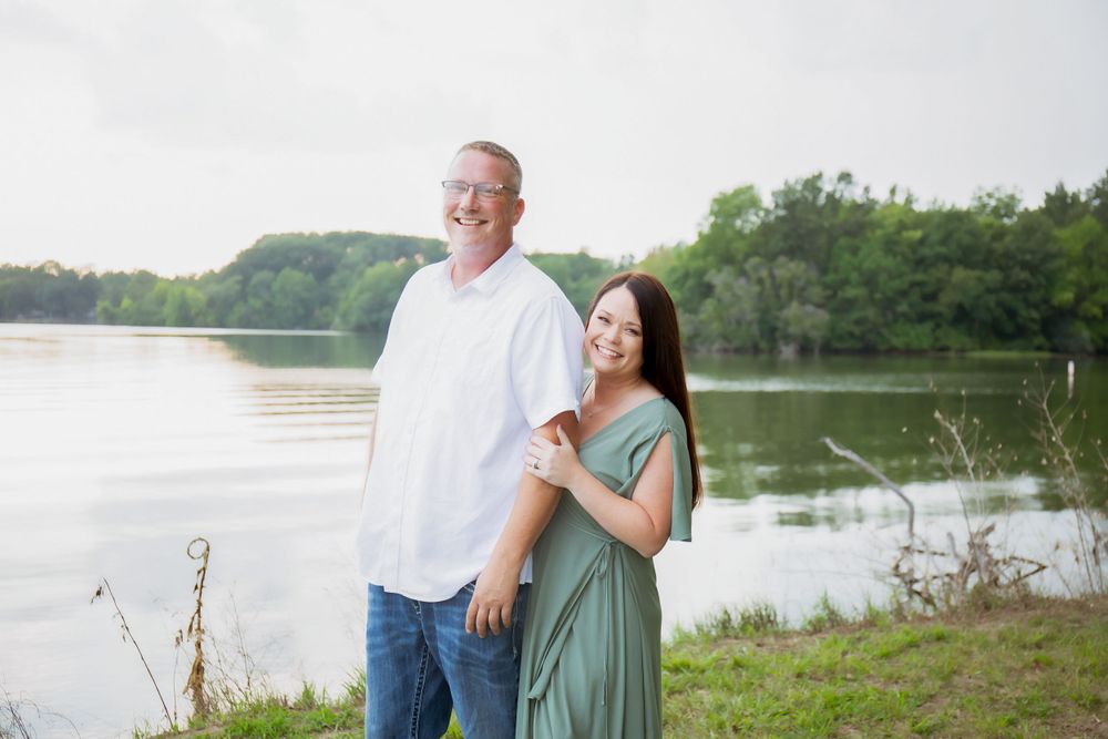 A couple poses together by a serene lake during a summer photoshoot.