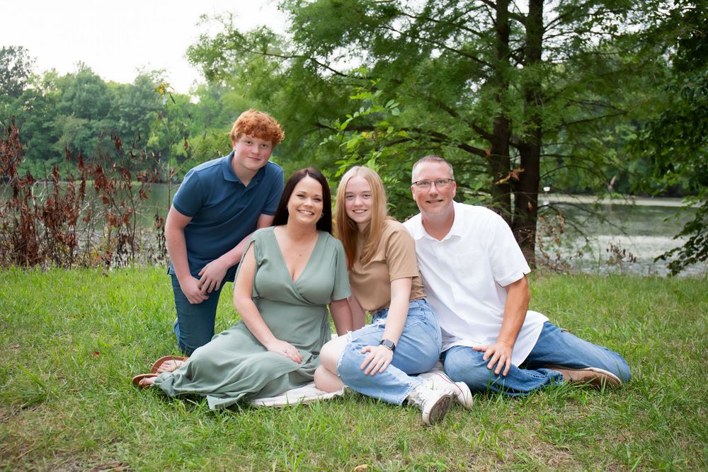 A family group sitting together on grass for a casual outdoor portrait by a lake.