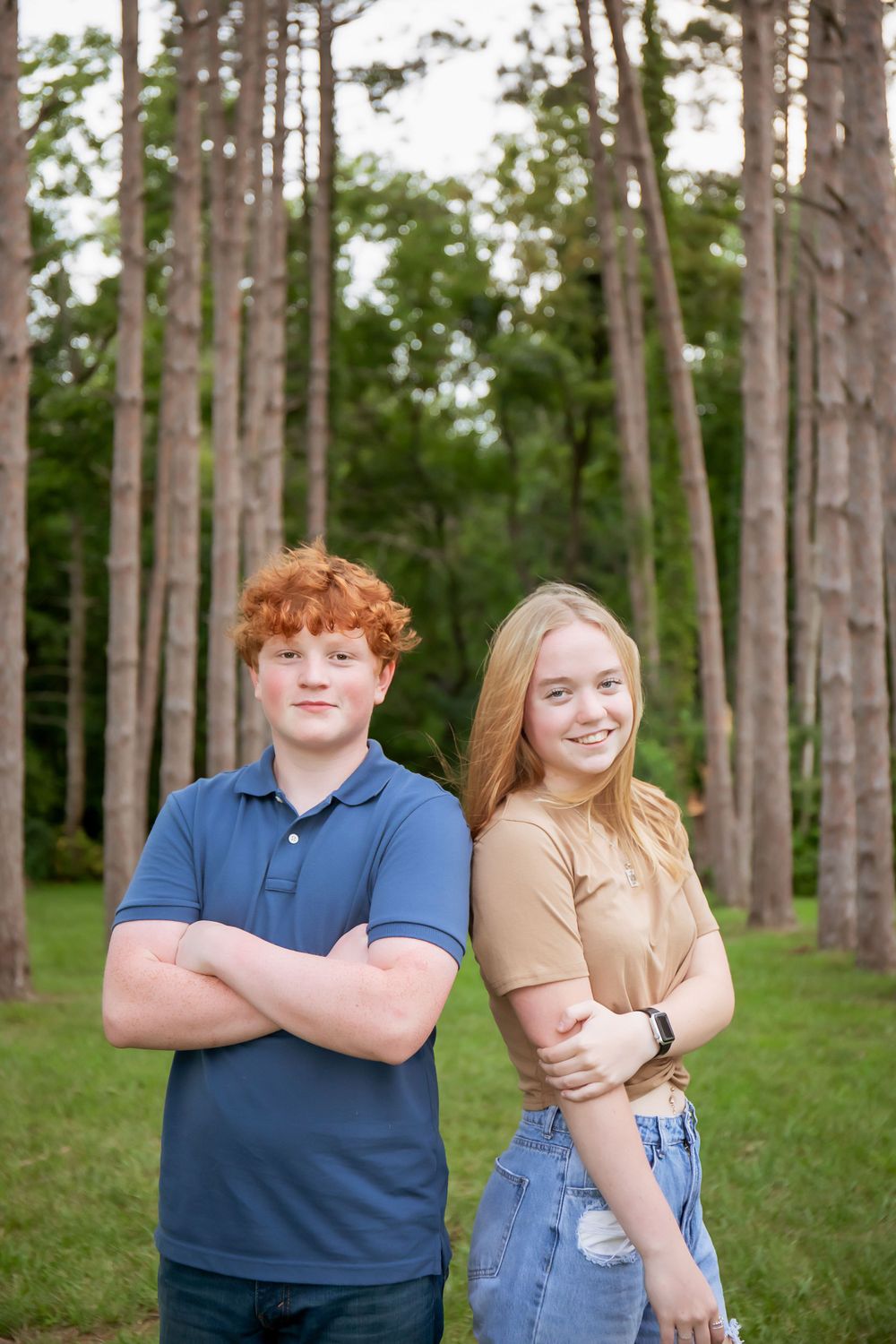 Two young people posing back-to-back in a scenic pine forest setting.