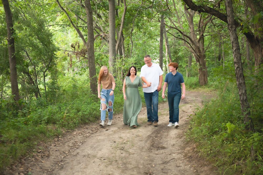Family of four walking together on a nature trail surrounded by lush green trees.