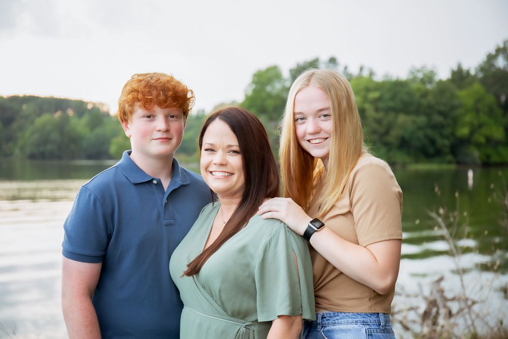 Three people pose close together for a casual outdoor portrait by a lake.