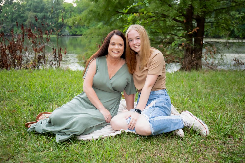 Two people sitting on grass by a lake during a summer photo session.
