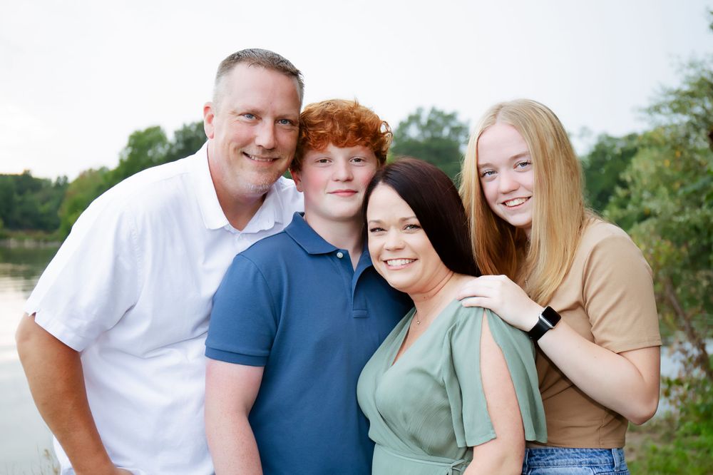 A cheerful family group photo taken outdoors with a lake in the background.