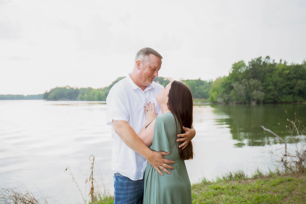 An intimate couple's portrait by a lakeside with trees in the background.