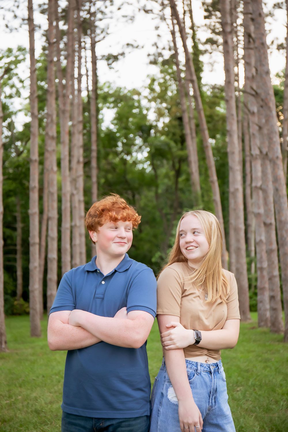 Two people smiling and posing casually in a serene pine forest.