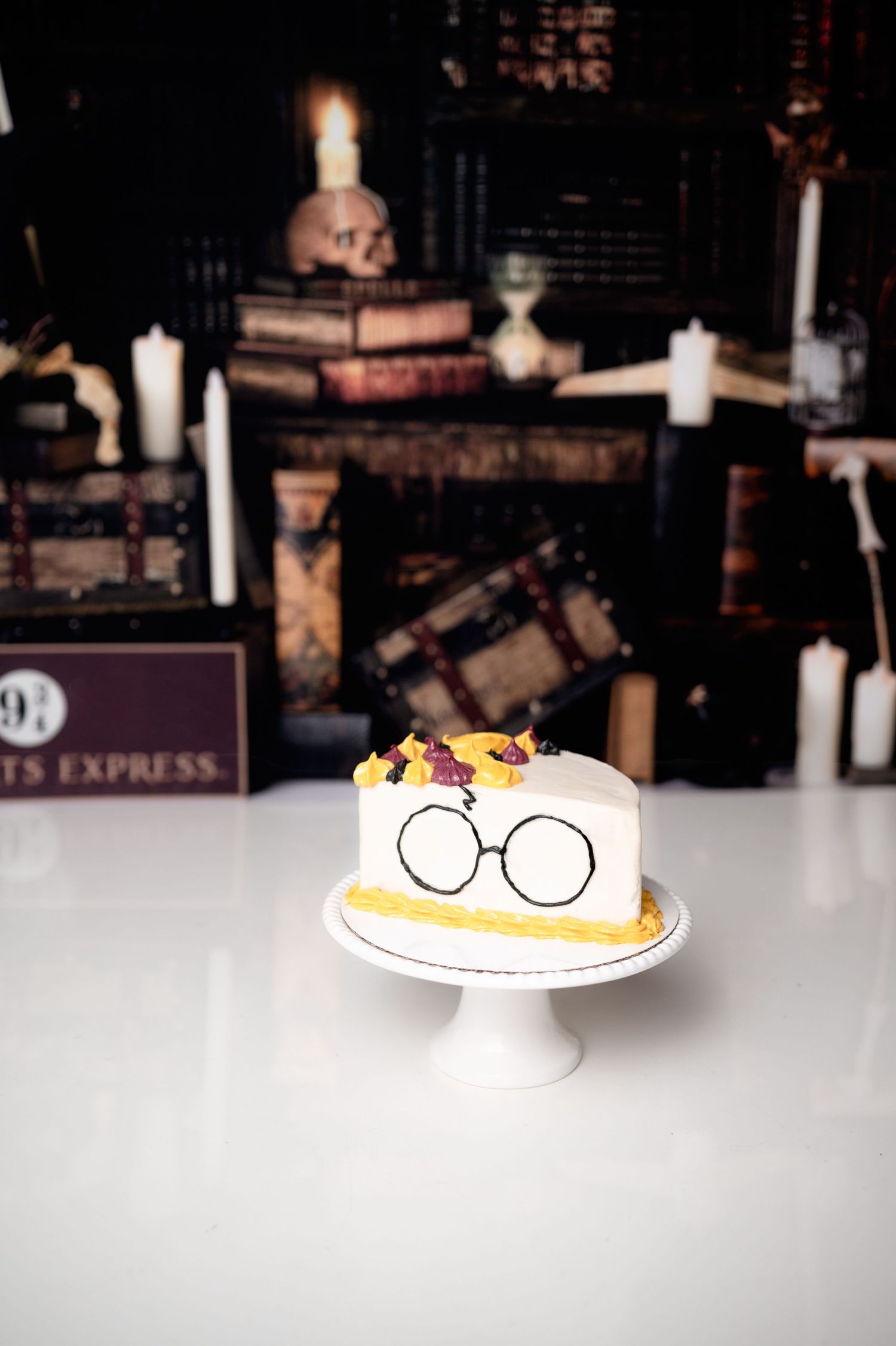 Harry Potter themed cake with glasses decoration on white pedestal.