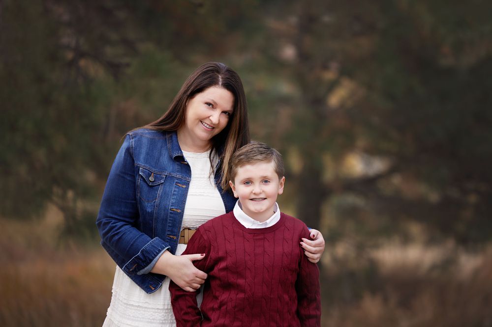 Portrait of parent and child wearing sweaters outdoors with natural fall background.