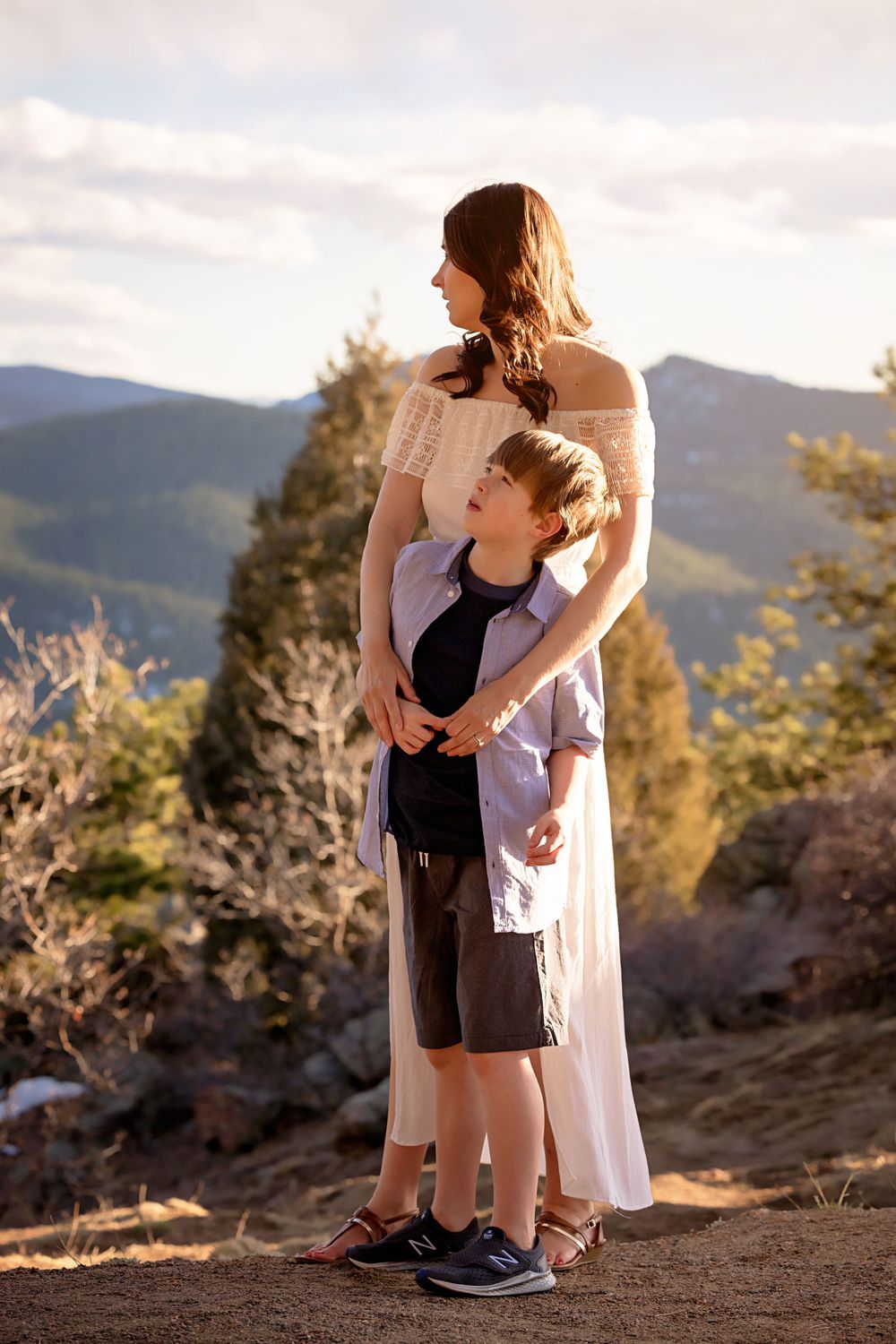 Mother and child embracing while standing on mountain trail overlooking scenic valley view.