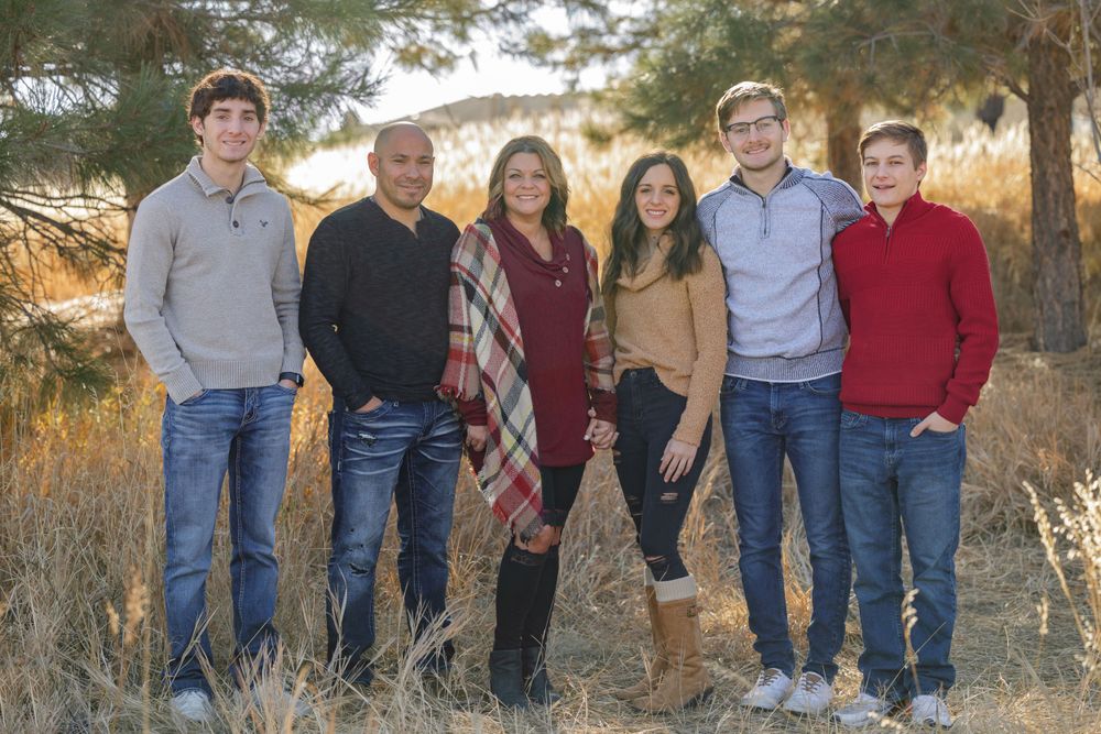 Group portrait in casual attire standing together in a grassy field at golden hour.