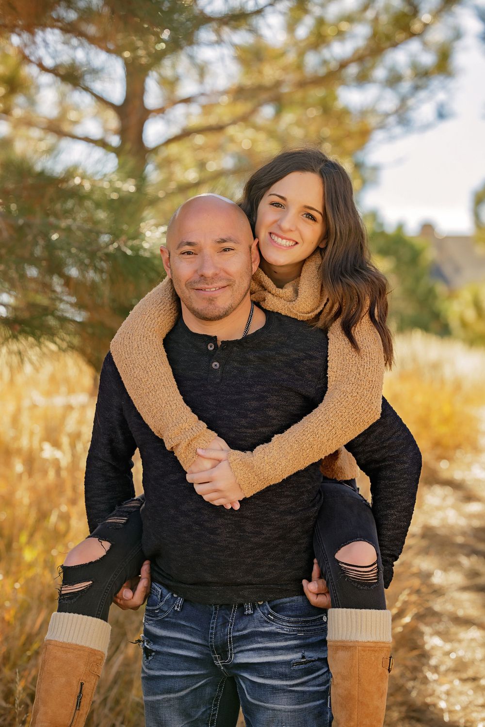 Couple embracing in piggyback pose against autumn mountain backdrop.