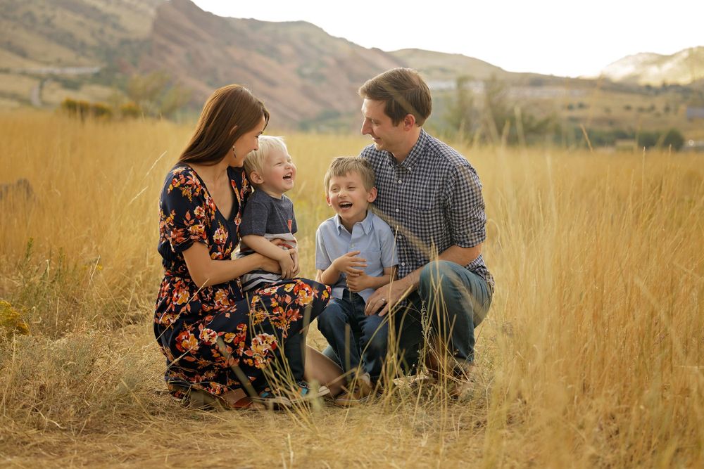 Family with young children laughing together in golden mountain field at sunset.