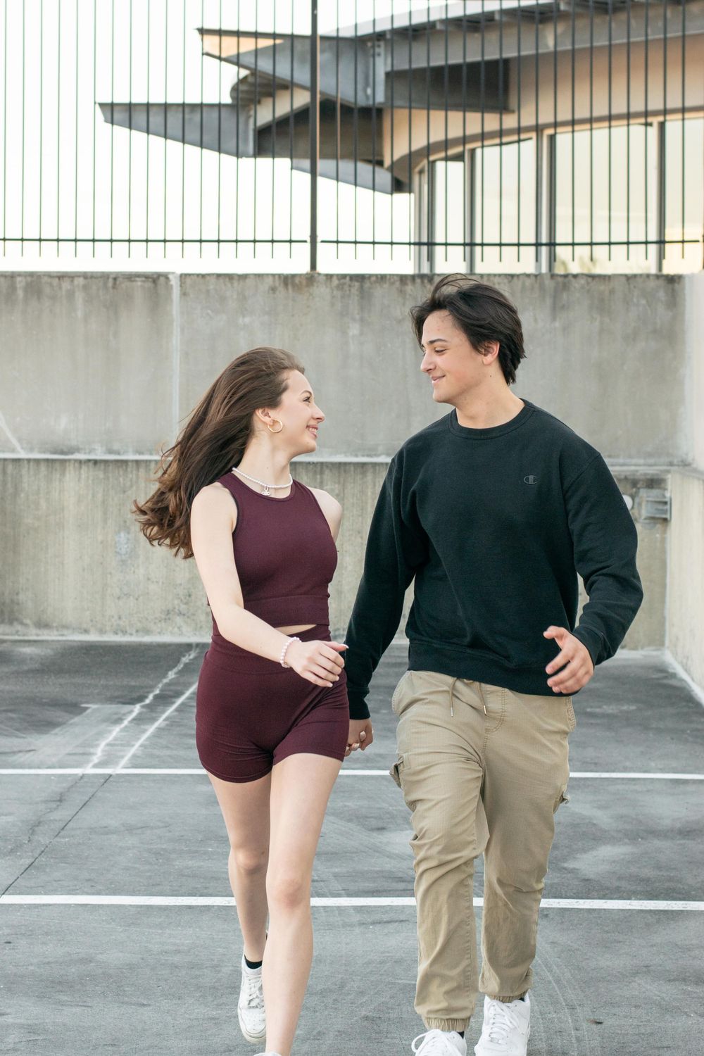 Couple in casual attire walking and laughing together in parking lot.