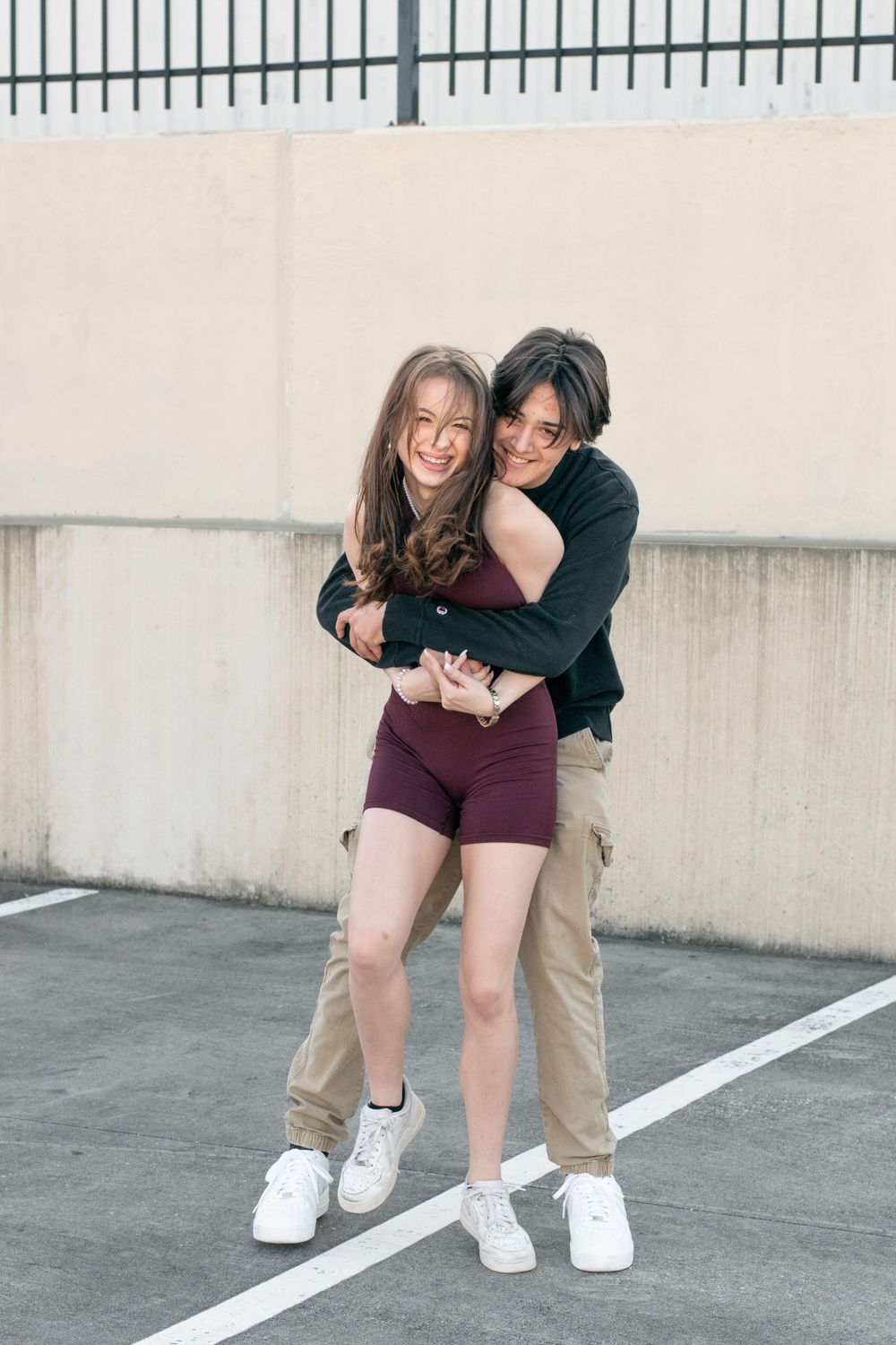 Two people share a playful embrace while standing on a parking lot line.