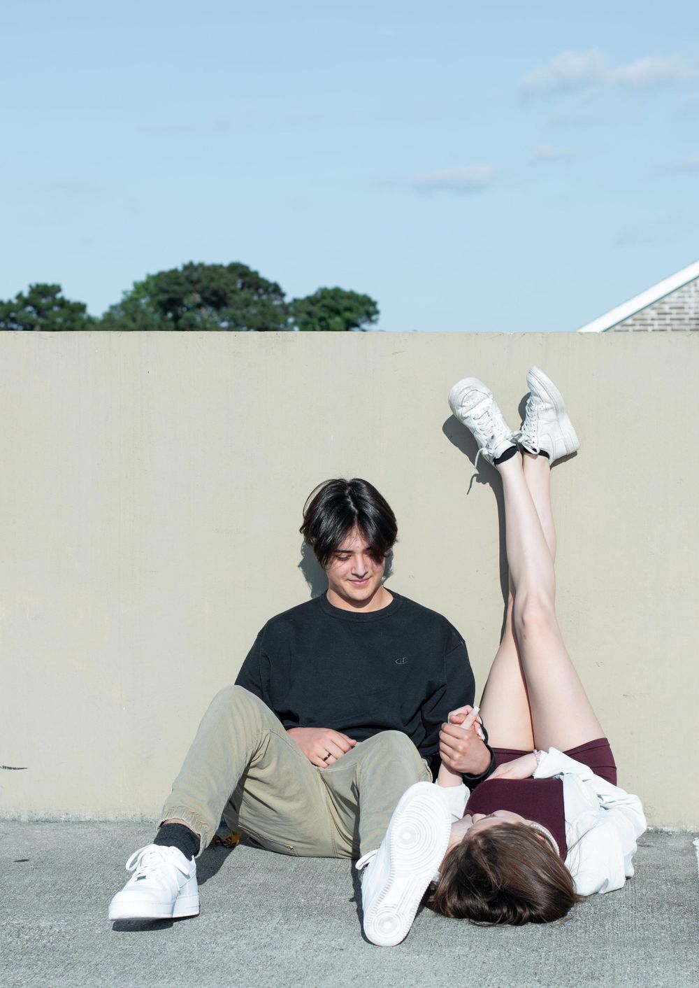 A casual photo shoot with two people in a parking structure showing a fun lying down pose.
