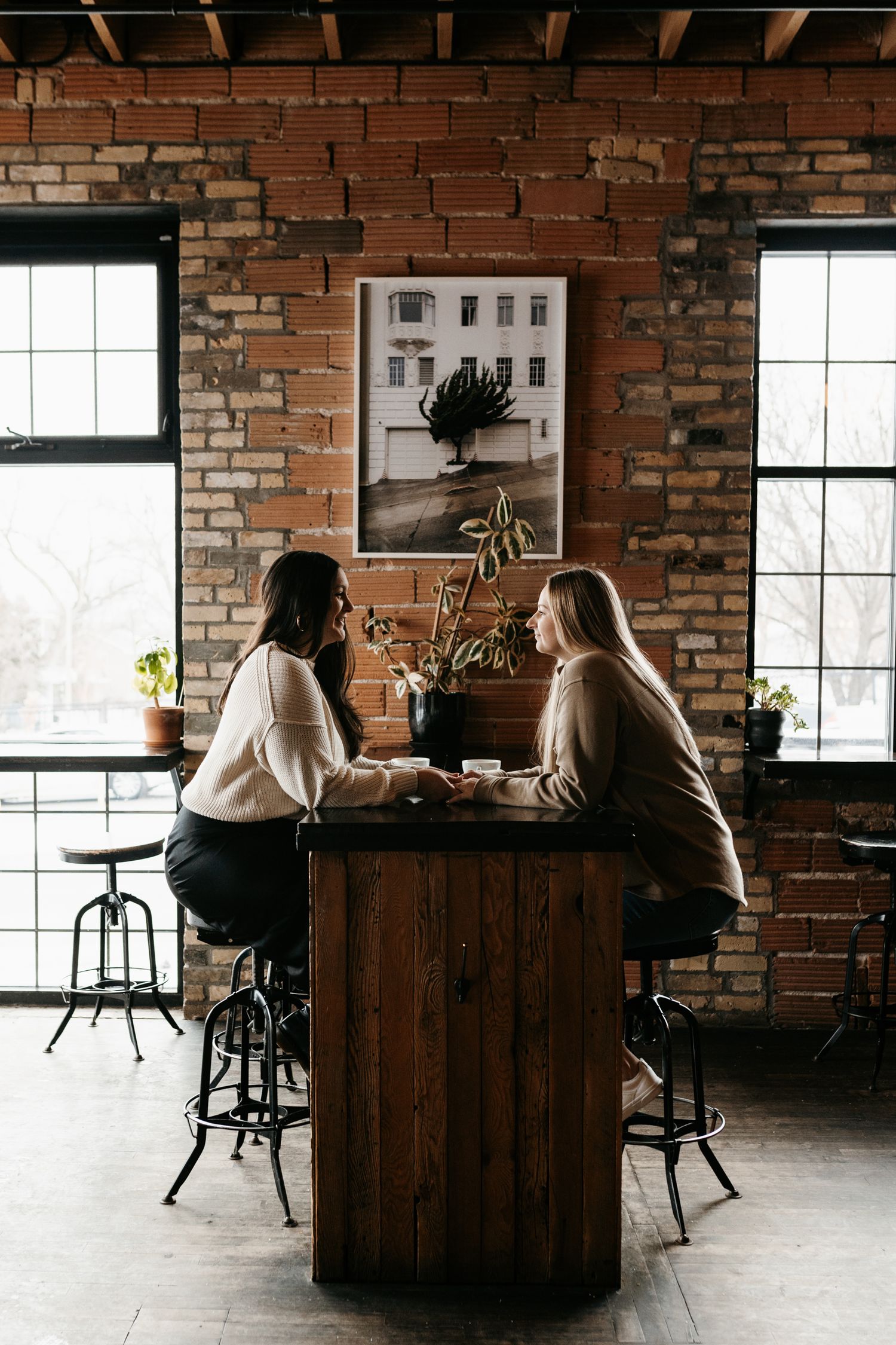 Two people enjoying coffee at a wooden table with exposed brick walls and large windows.