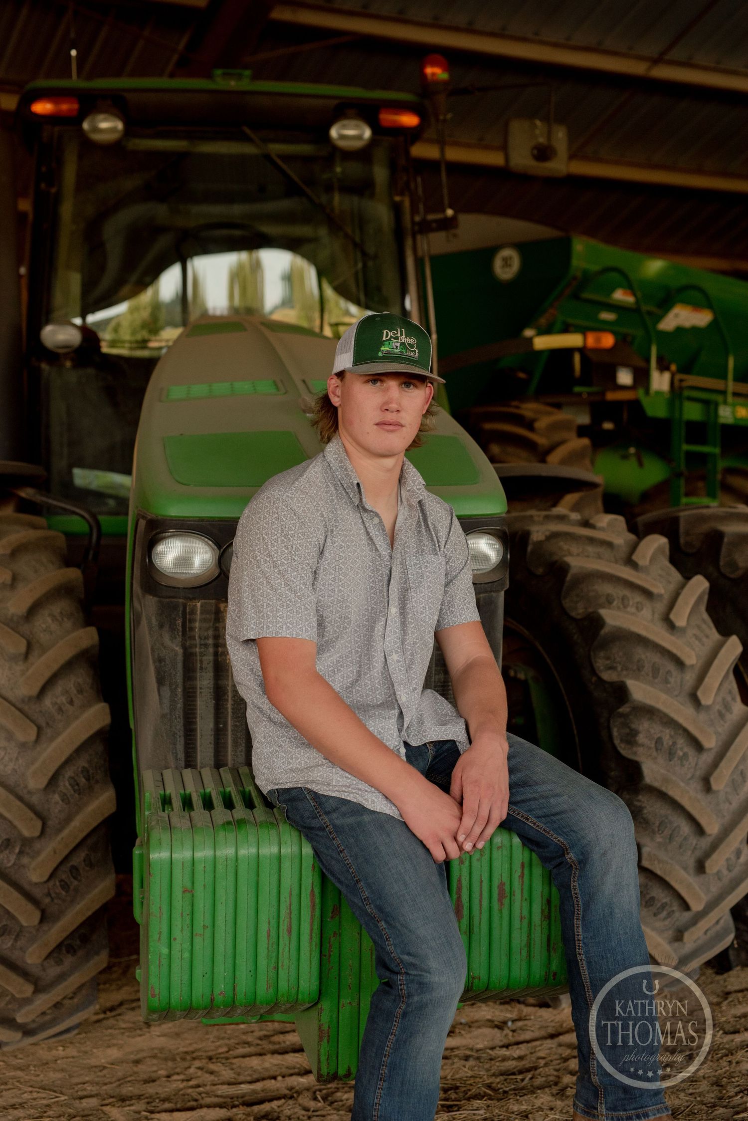 Farmer sits on a green John Deere tractor wearing a baseball cap and casual attire.