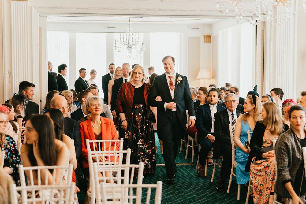 Elegant ballroom with crystal chandelier and guests seated in white chairs for a ceremony.
