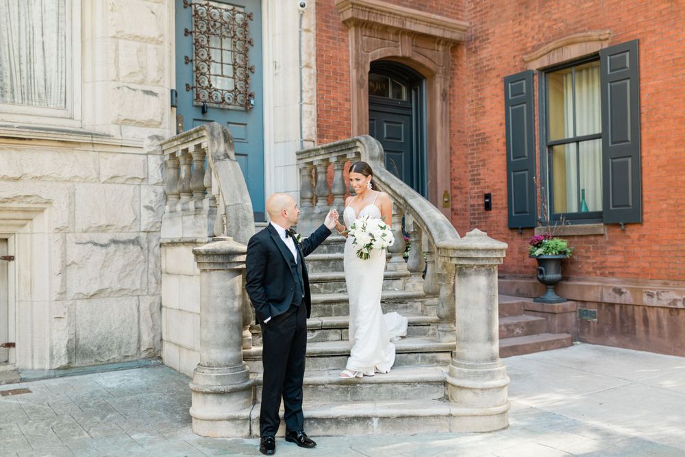 Wedding couple poses on historic stone steps of a brick building with ornate architecture.