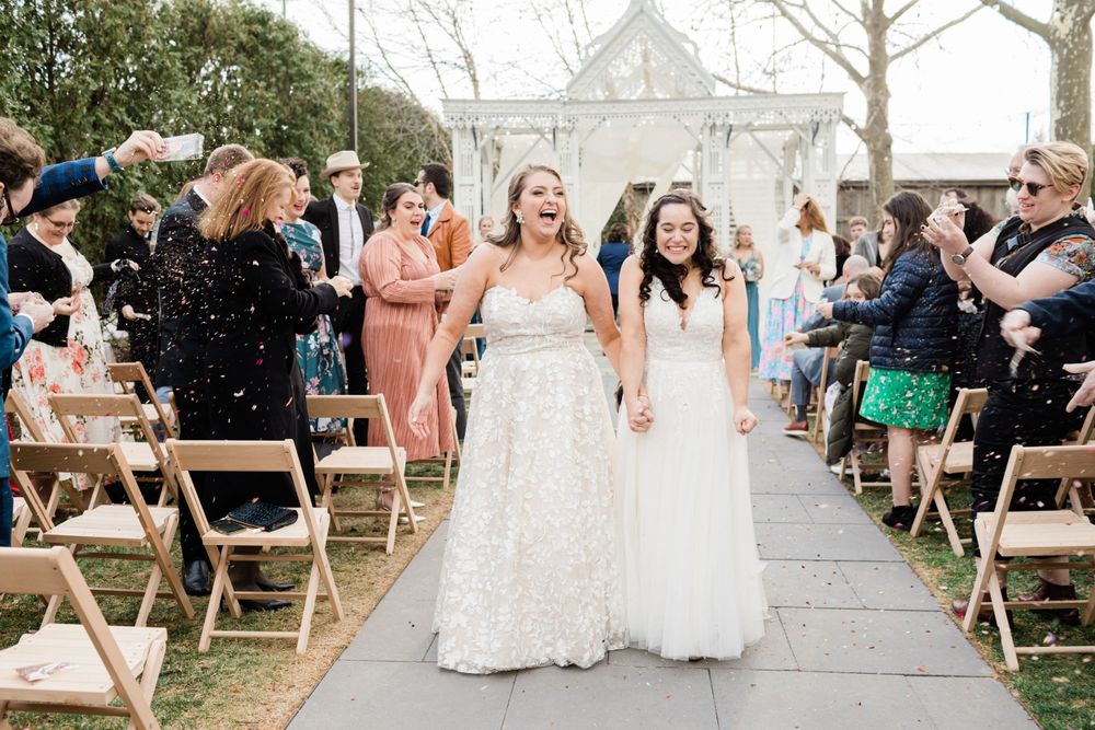 Joyful wedding celebration with guests tossing confetti on outdoor ceremony path.
