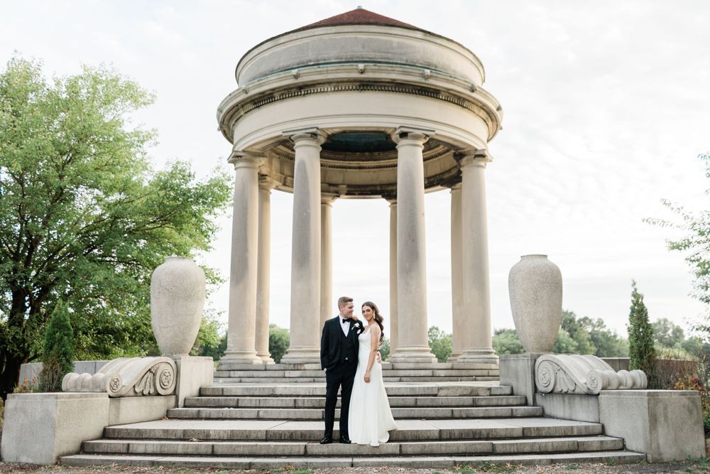 Wedding couple standing at classical white stone gazebo with columns.