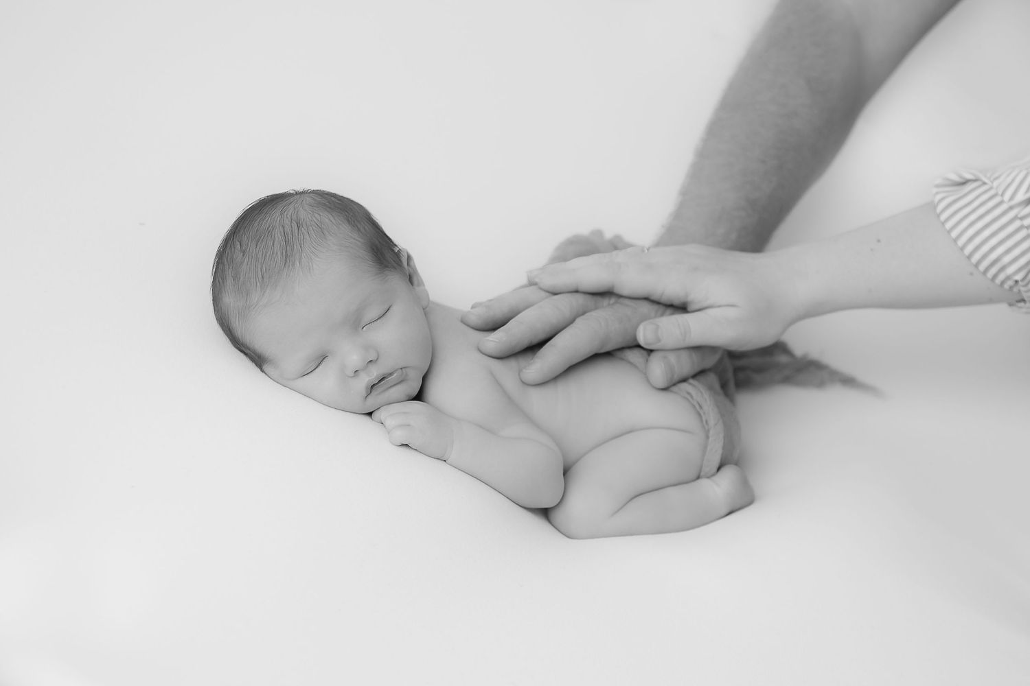 Black and white newborn photography with gentle supporting hands.