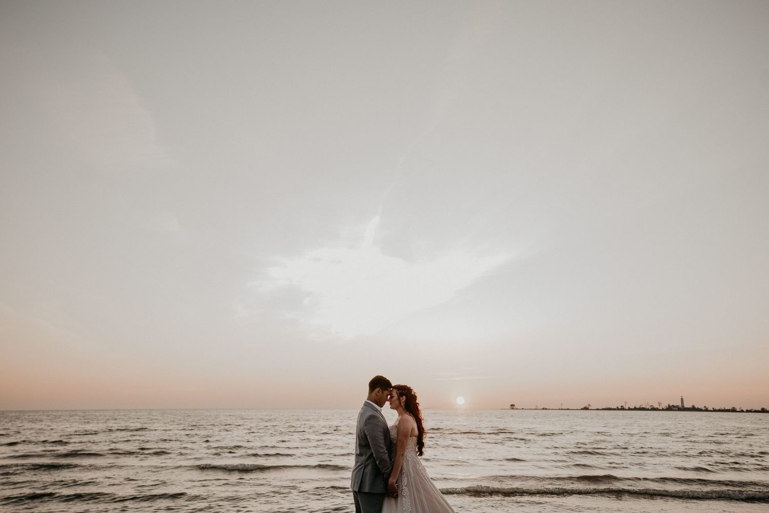 bride and groom touch foreheads in front of setting sun