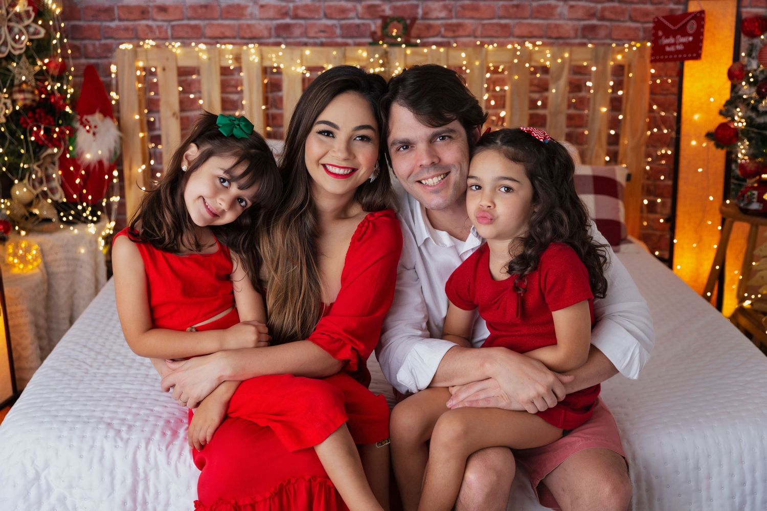 Family dressed in red and white poses for Christmas portrait with twinkling lights.