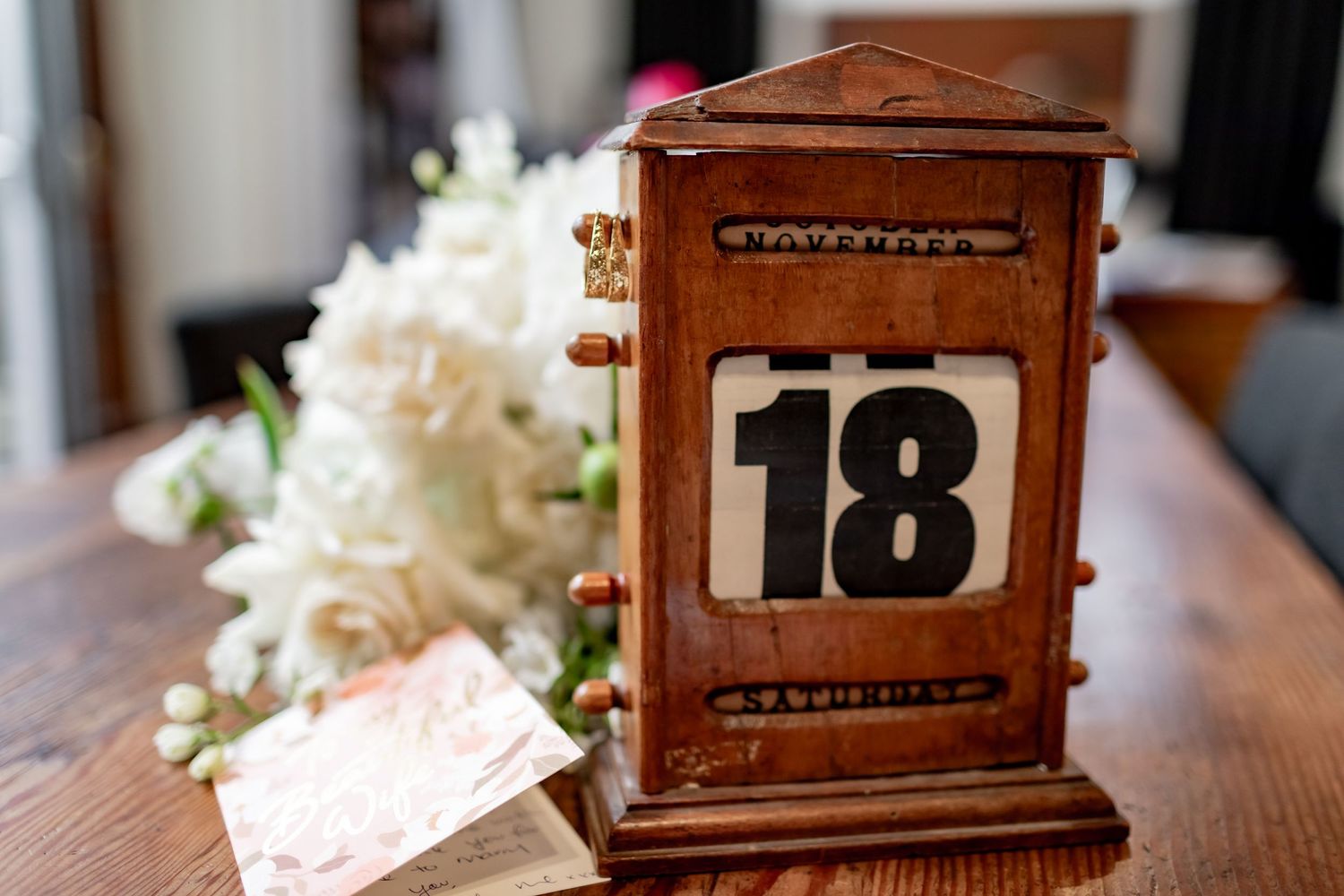A wooden calendar showing number 18 next to white flowers on a table.