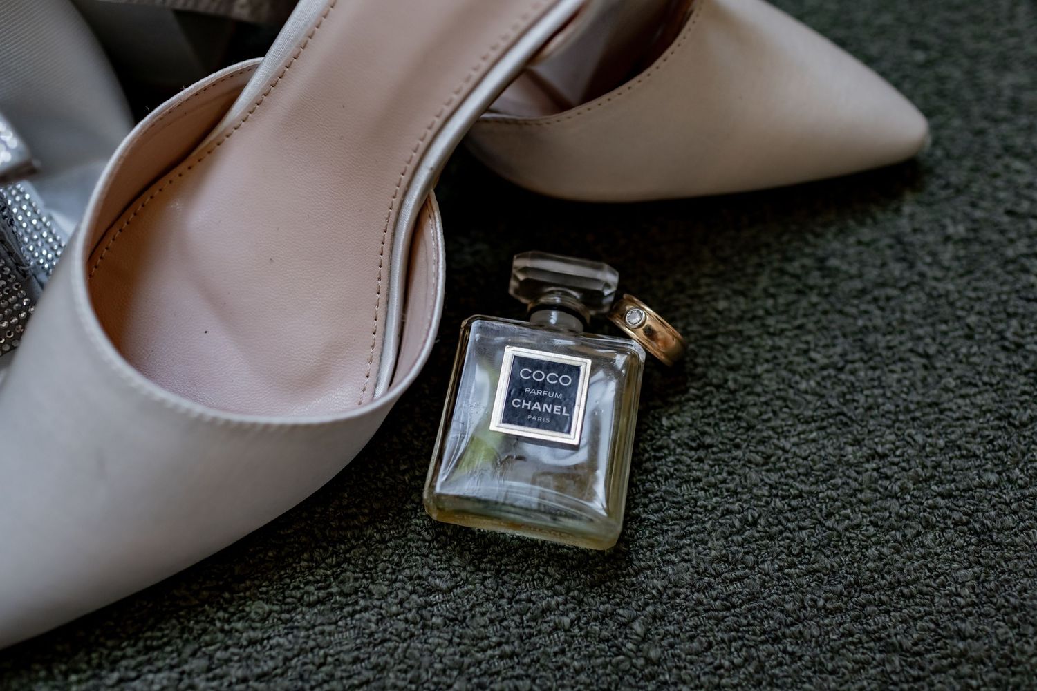 Elegant nude pumps and a glass perfume bottle arranged on a dark surface.
