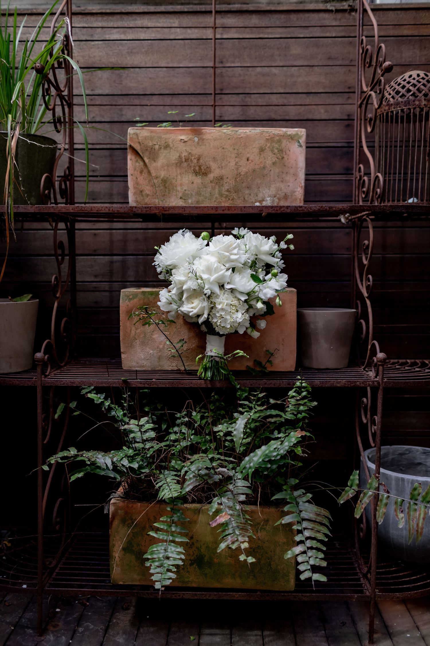 A rustic metal shelf display with white flowers and ferns arranged in vintage wooden boxes.