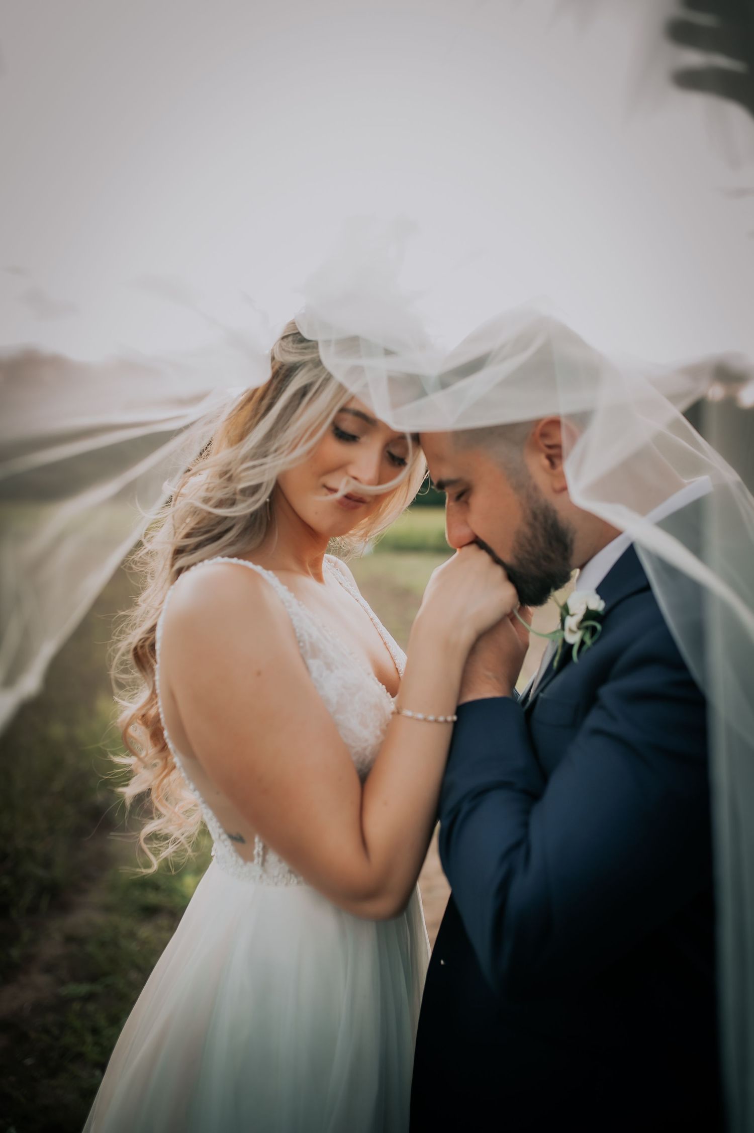 A romantic wedding portrait of a couple sharing an intimate moment under a veil in soft lighting.