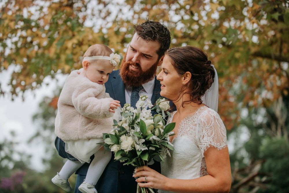 Family moment outdoors with wedding bouquet and autumn foliage in background.