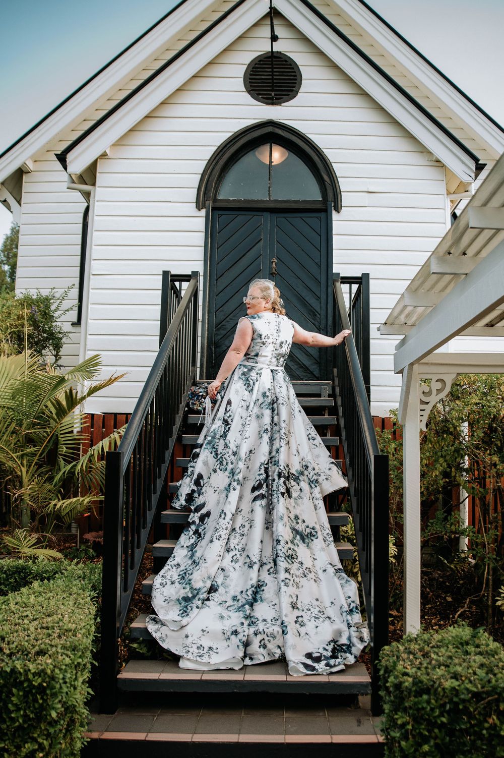 A stunning black and white floral wedding gown displayed on the steps of a white chapel with arched doorway.