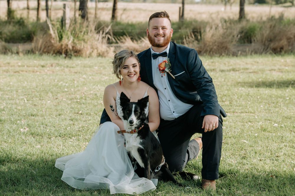 A couple poses with their Border Collie dog during their wedding photoshoot on a grassy field.
