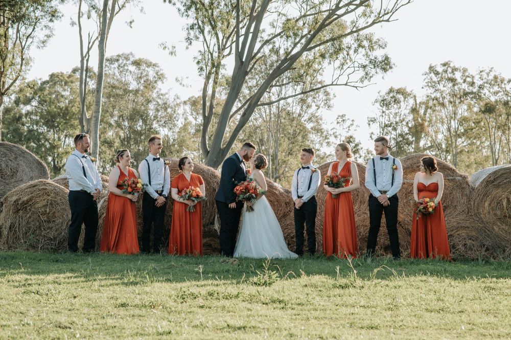 Wedding party poses in rust-colored dresses and dark suits against a backdrop of eucalyptus trees.