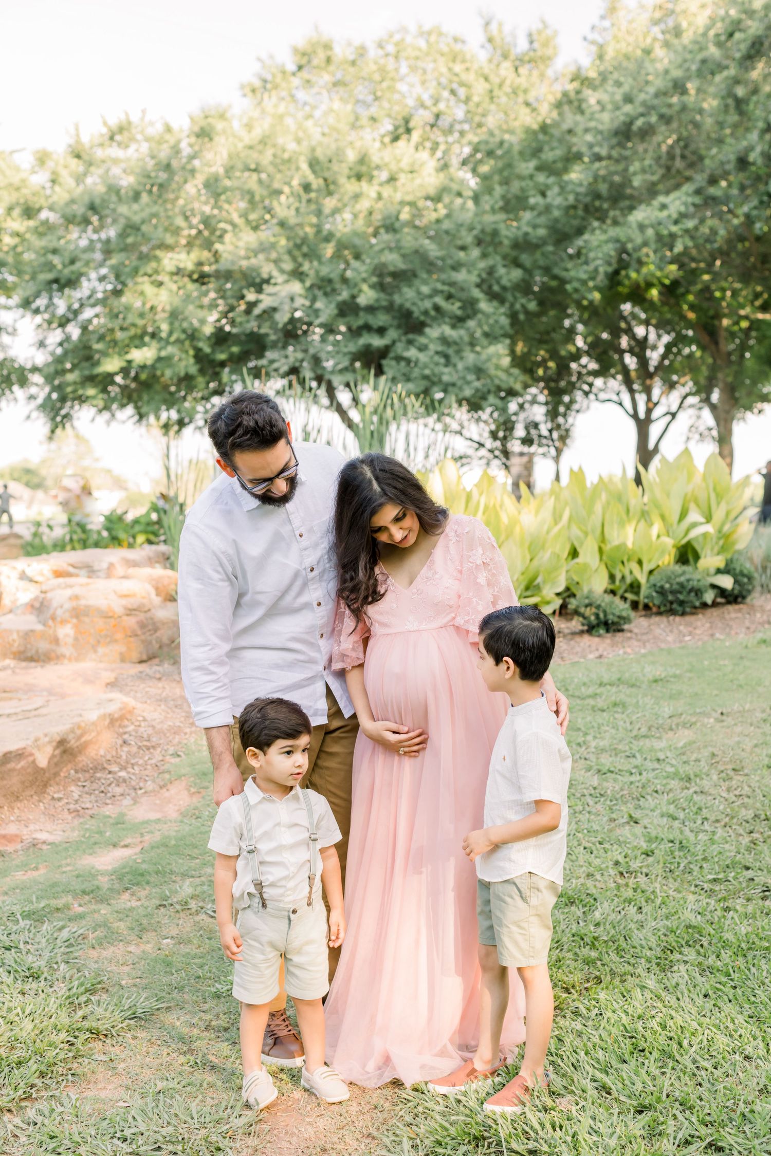 A family stands together on grassy ground with trees and landscaping behind them.