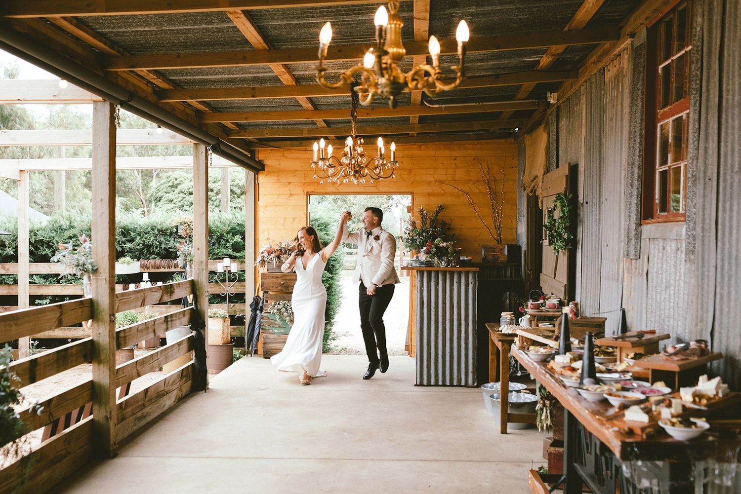 Wedding reception in rustic wooden venue with chandeliers and dessert display.