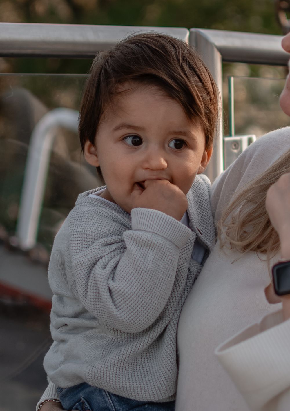 A small child in a gray sweater with a shy expression and finger in mouth.