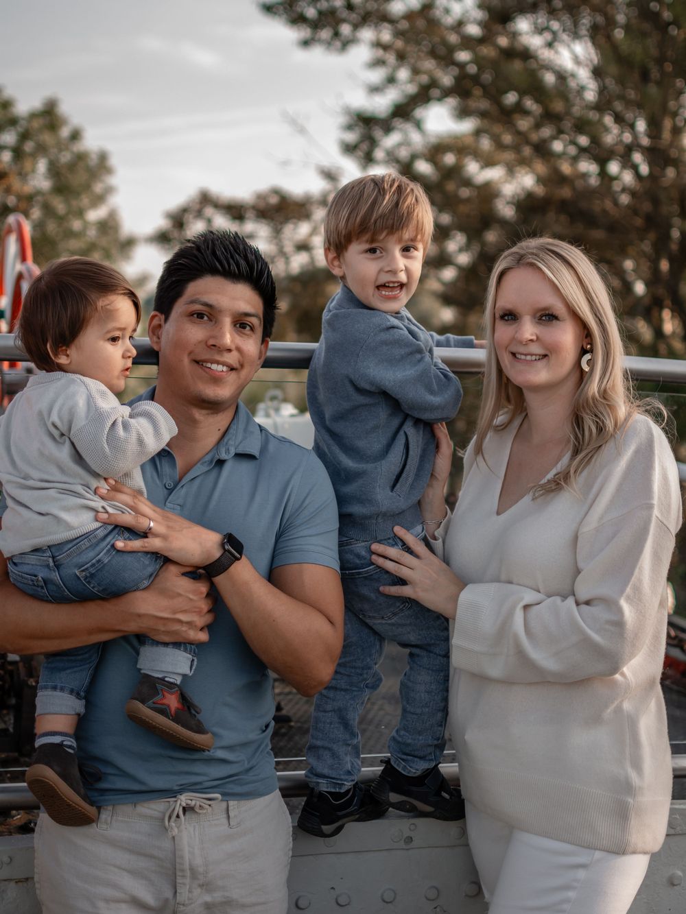 A family of four poses together outdoors wearing coordinated casual clothing.
