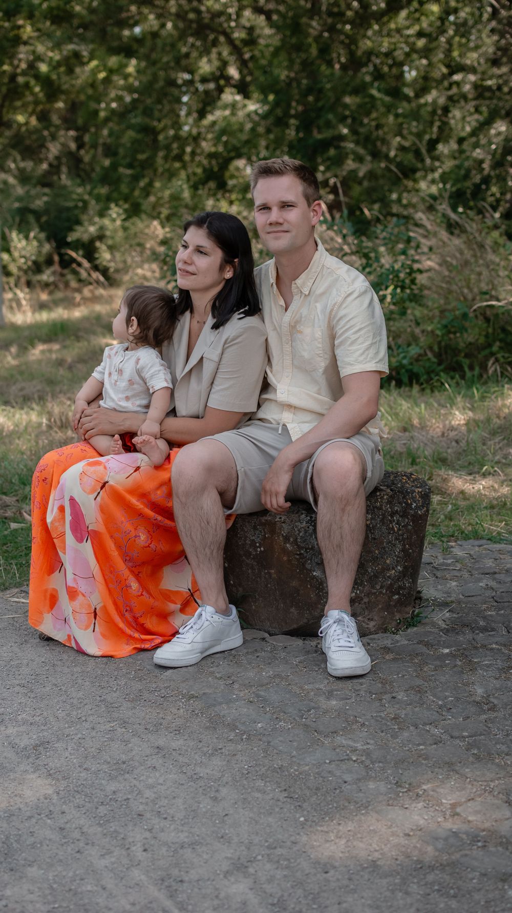 A family sitting together on a rock outdoors, with vibrant orange skirt adding a pop of color.