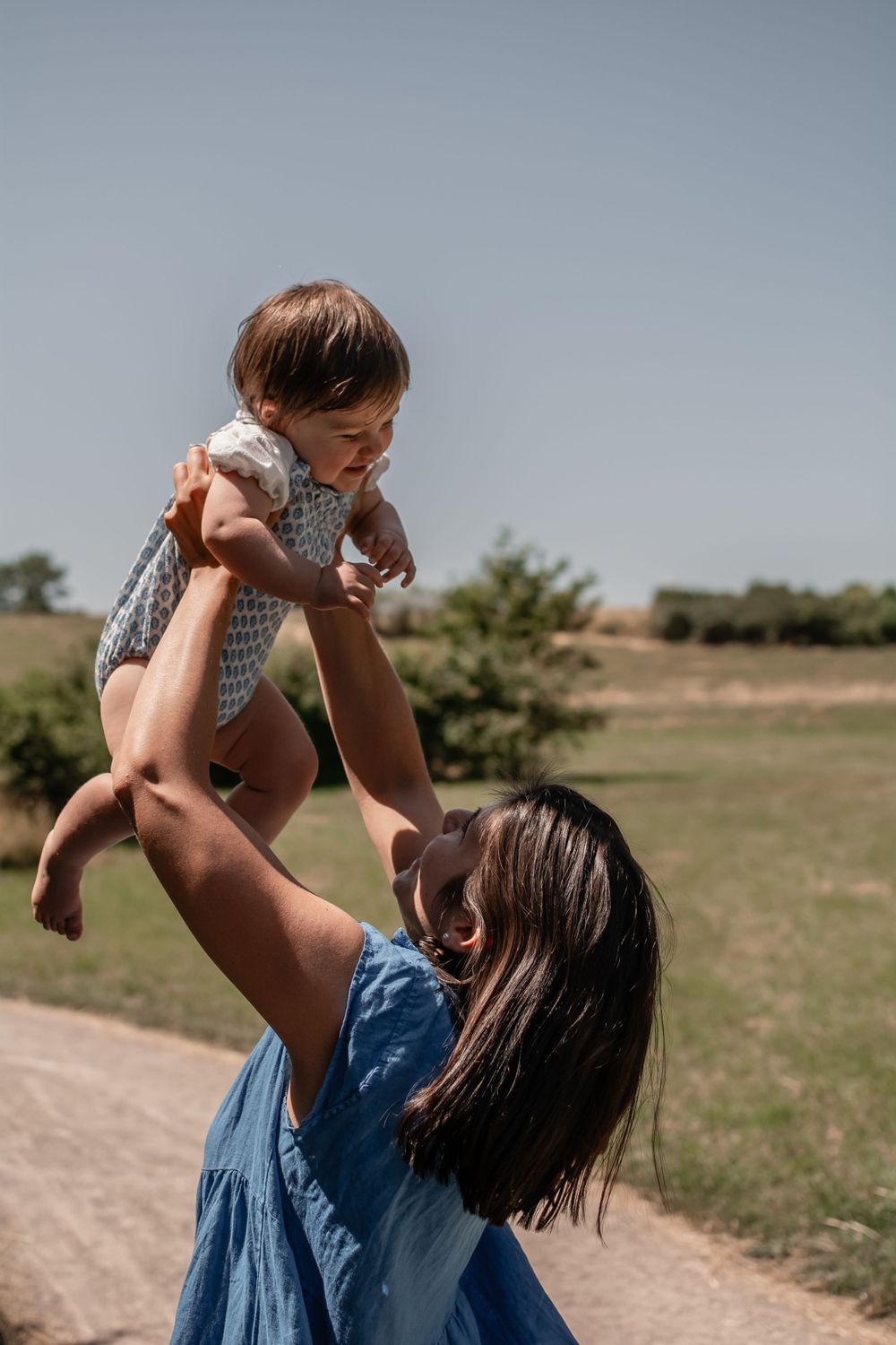 A joyful moment outdoors as a baby in a polka dot outfit is lifted high into the air on a sunny day.