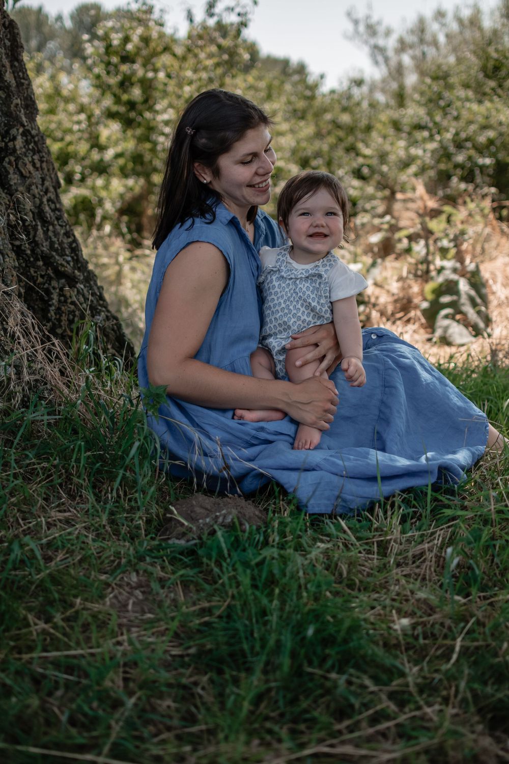 A tender outdoor moment under a tree with laughter and smiles on a sunny afternoon.