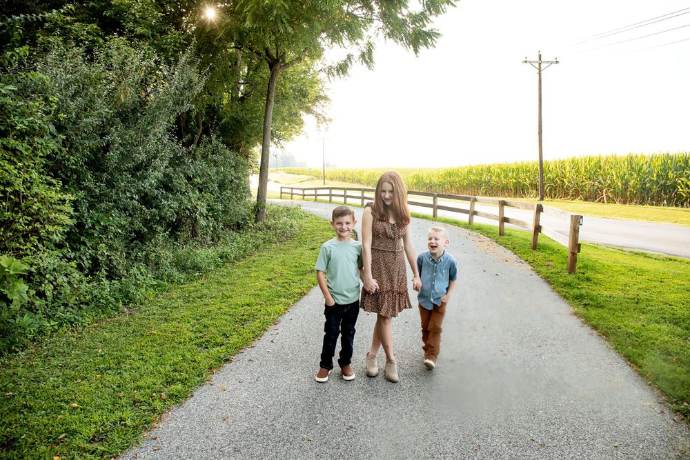 Three people stand together on a rural path with cornfields in background.