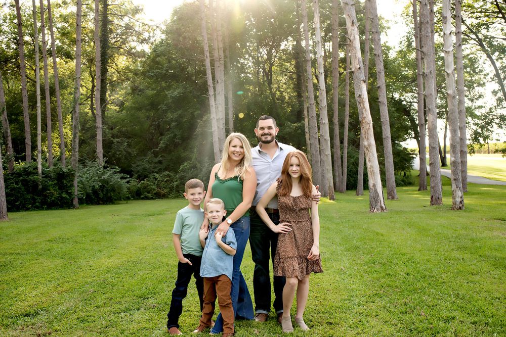 Family and their dog pose together in a scenic wooded area during golden hour.